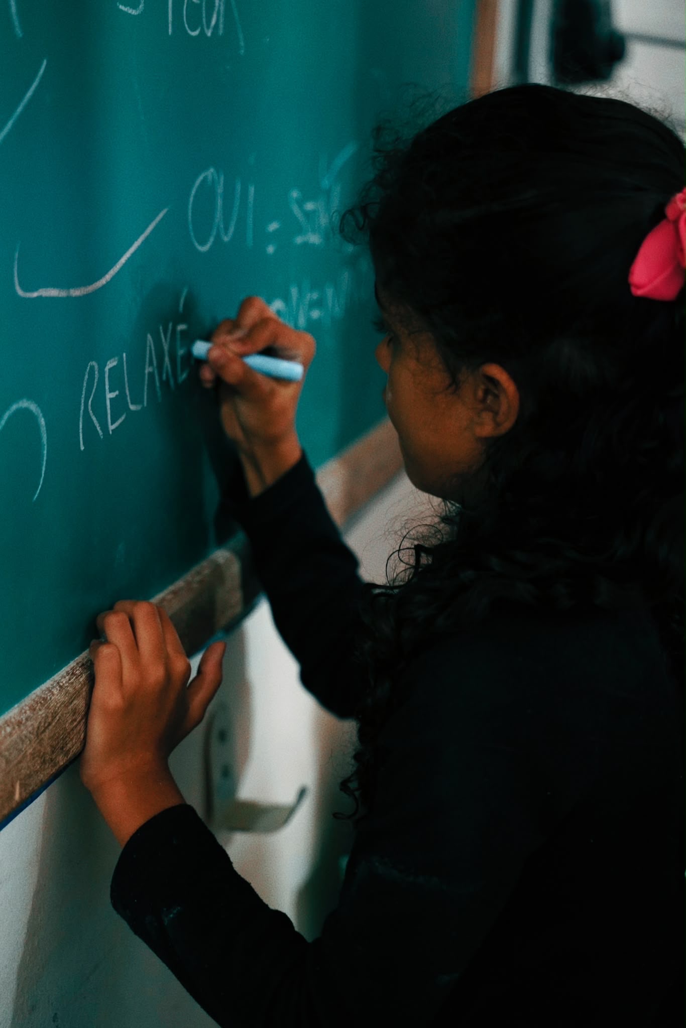 A girl writes in English on a green chalkboard during a class.