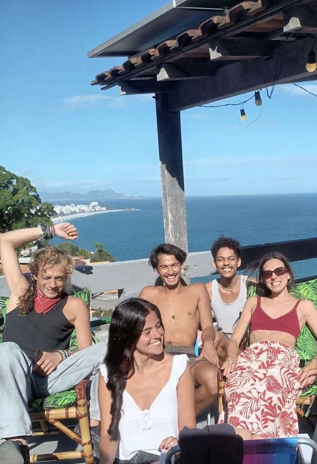Housemates relax together on the rooftop terrace, with the sea and the coastline behind them.