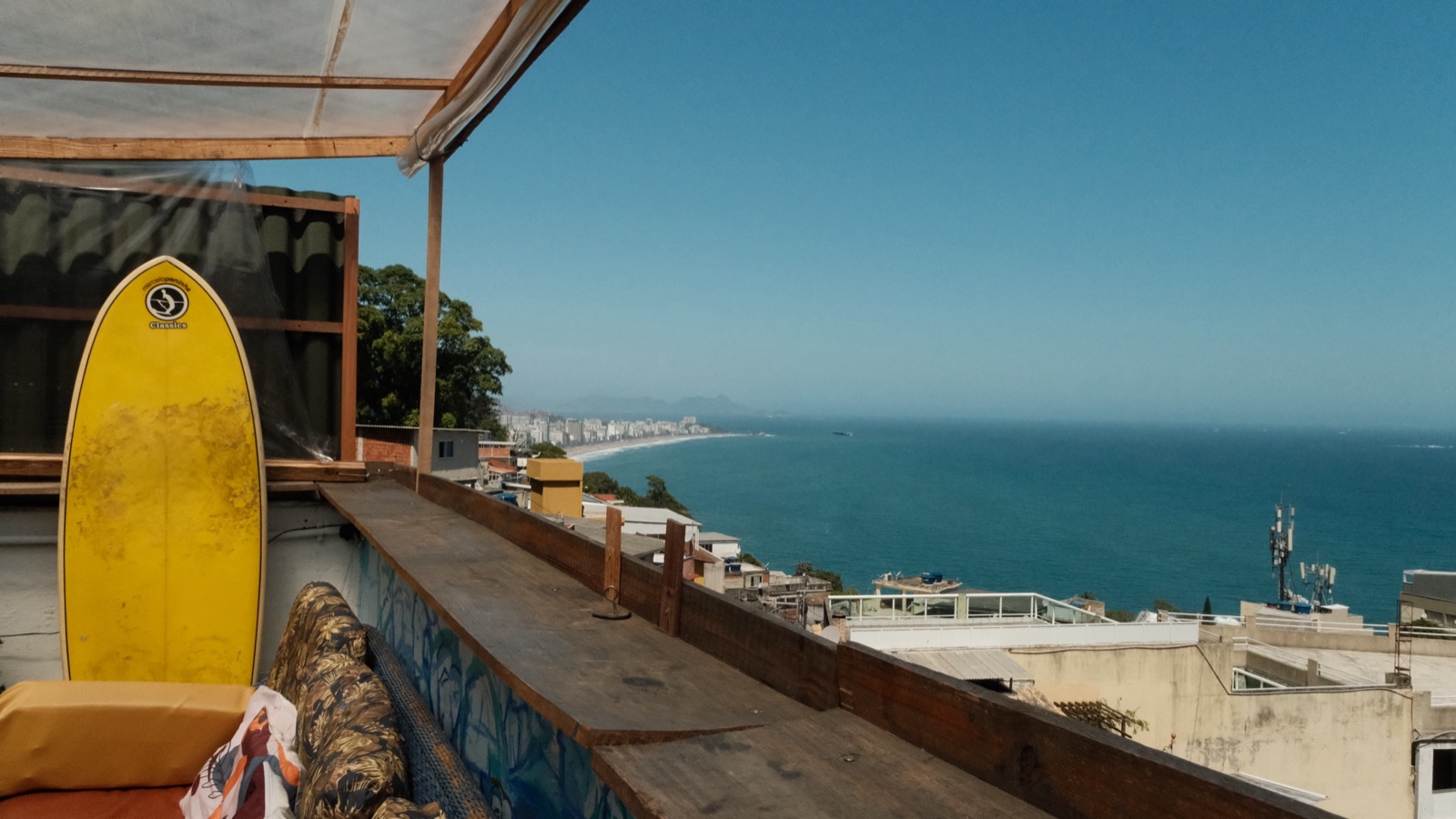 The rooftop terrace in Vidigal, with a yellow surfboard leaning against the wall and the sea and Leblon beyond.