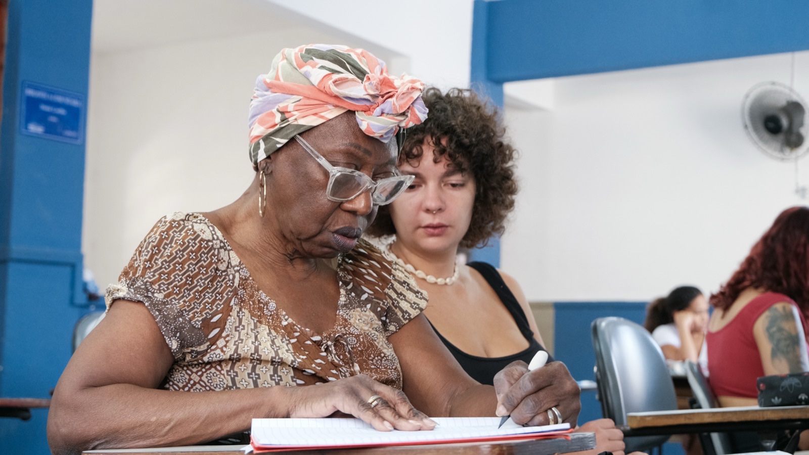 A local educator and an international student work through notes together at a classroom desk.
