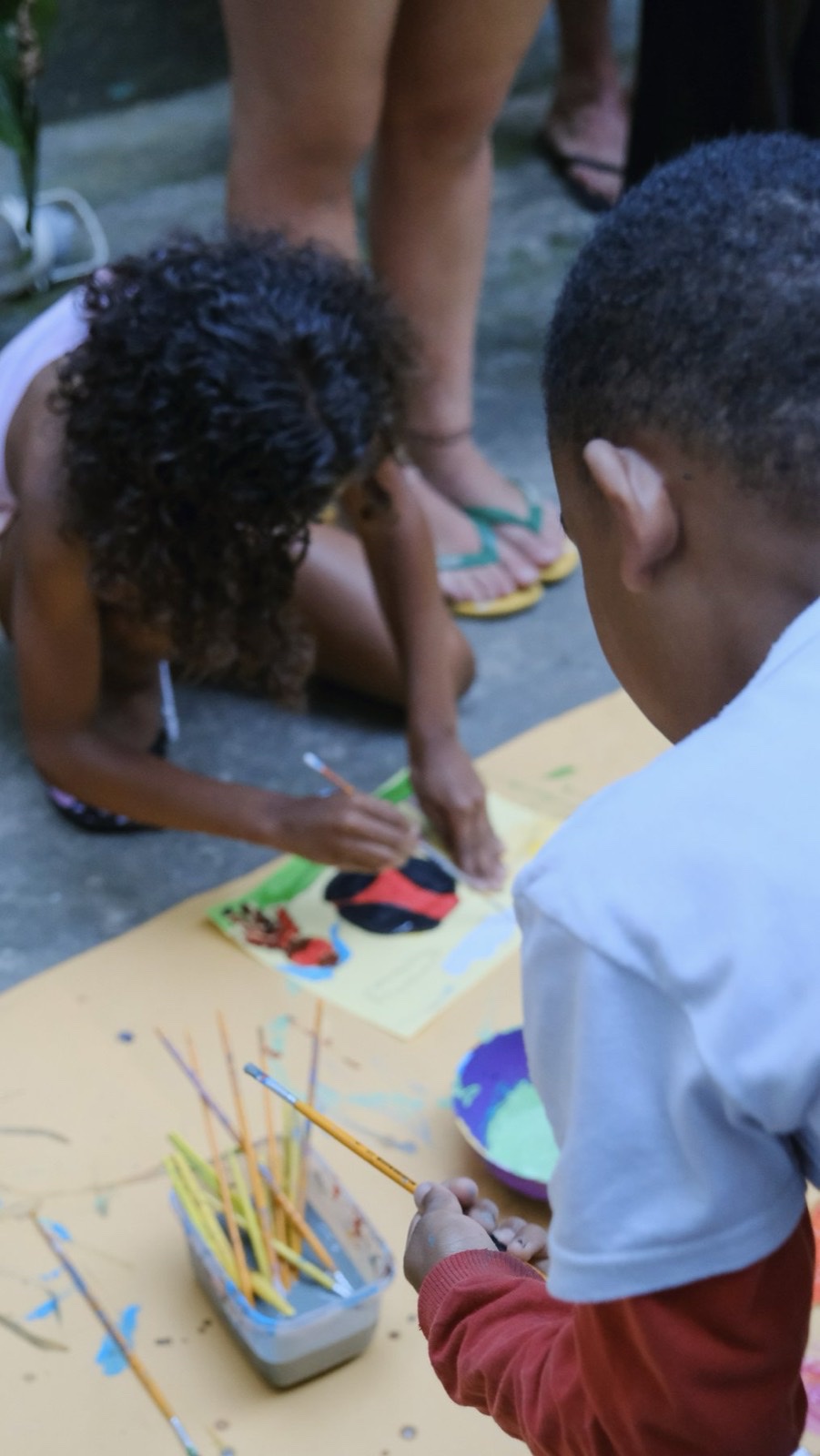 Close-up of children painting with brushes and bottles of colour.