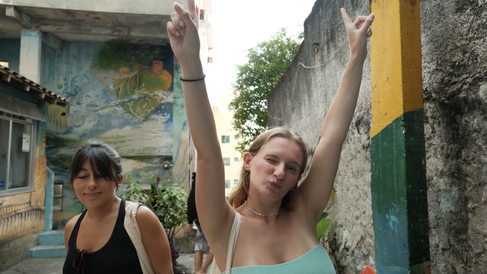Two friends in a painted Vidigal alley, one throwing her arms up in celebration.