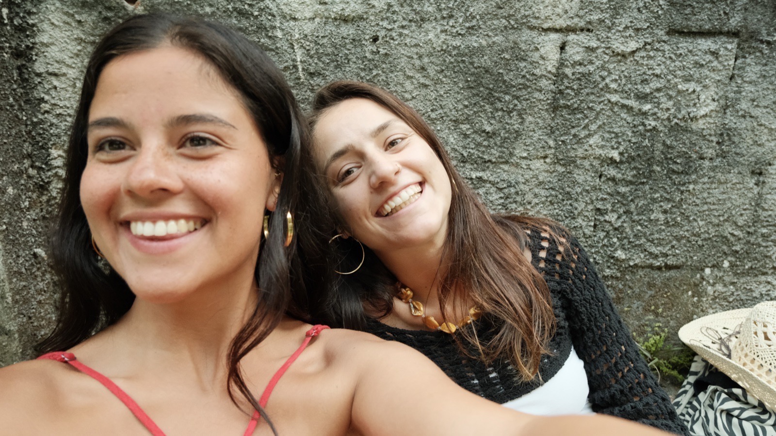 Two friends lean in together, laughing, in front of a stone wall in Vidigal.