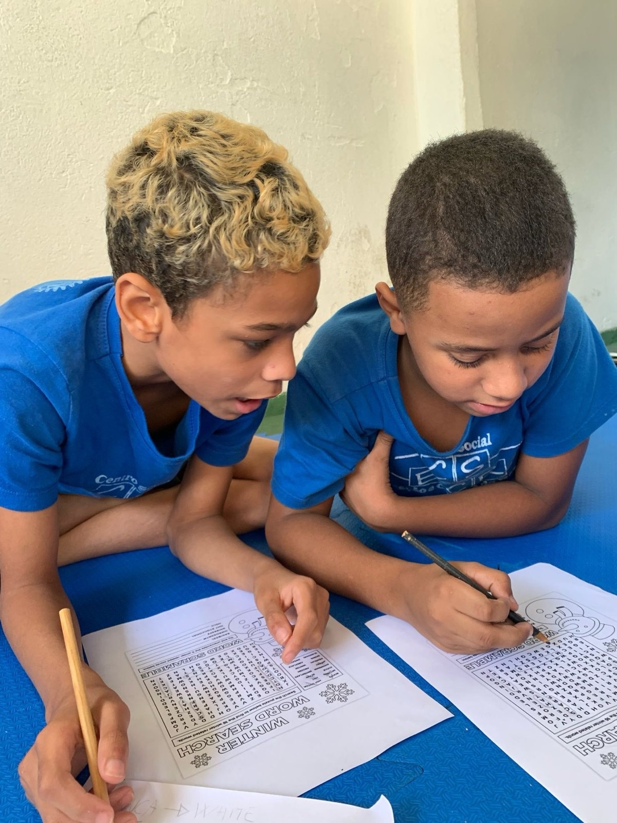 Two boys writing together in an English workbook.