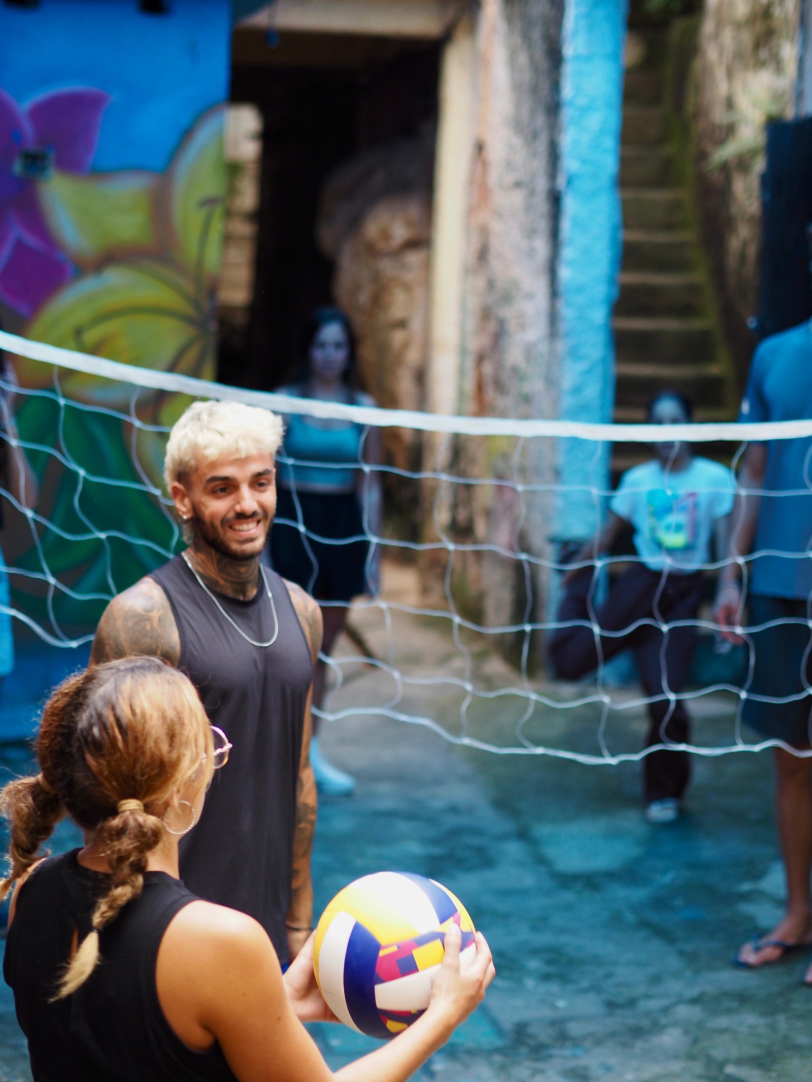 Children gather around a volleyball net strung across an alley.
