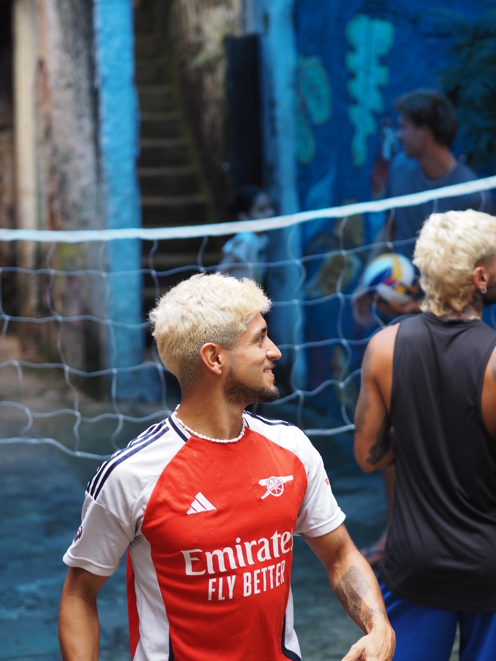 A volunteer in a football shirt plays volleyball with children in a Vidigal alley.