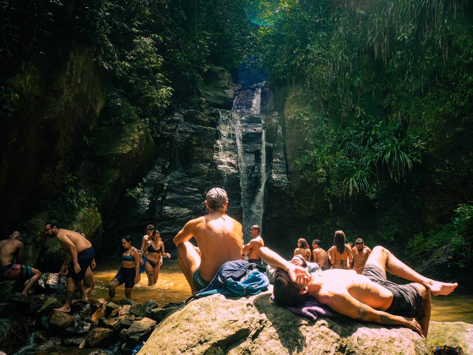 Volunteers relax and swim together at a waterfall pool in the forest.