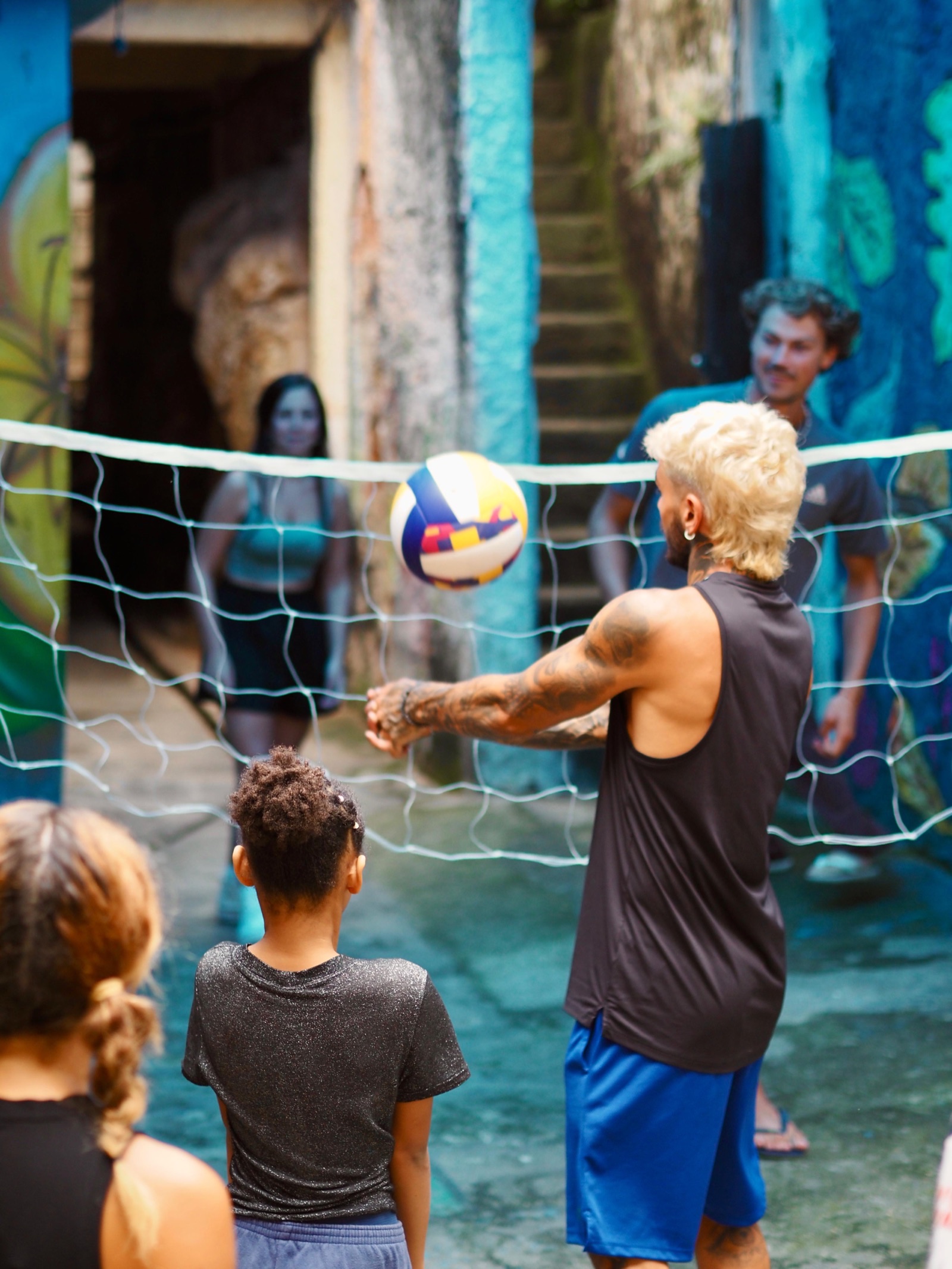 A volunteer sets a volleyball over a net to children in a Vidigal alley.