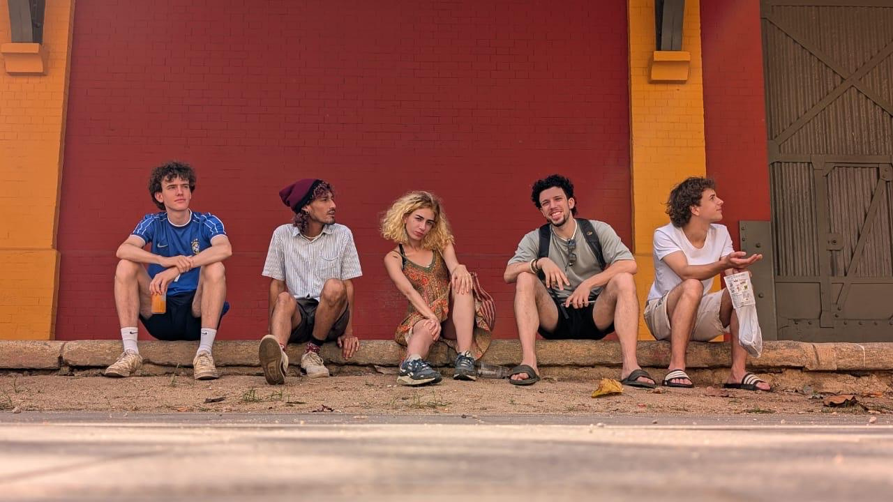 Four young people sitting together on a low wall in front of a red building.